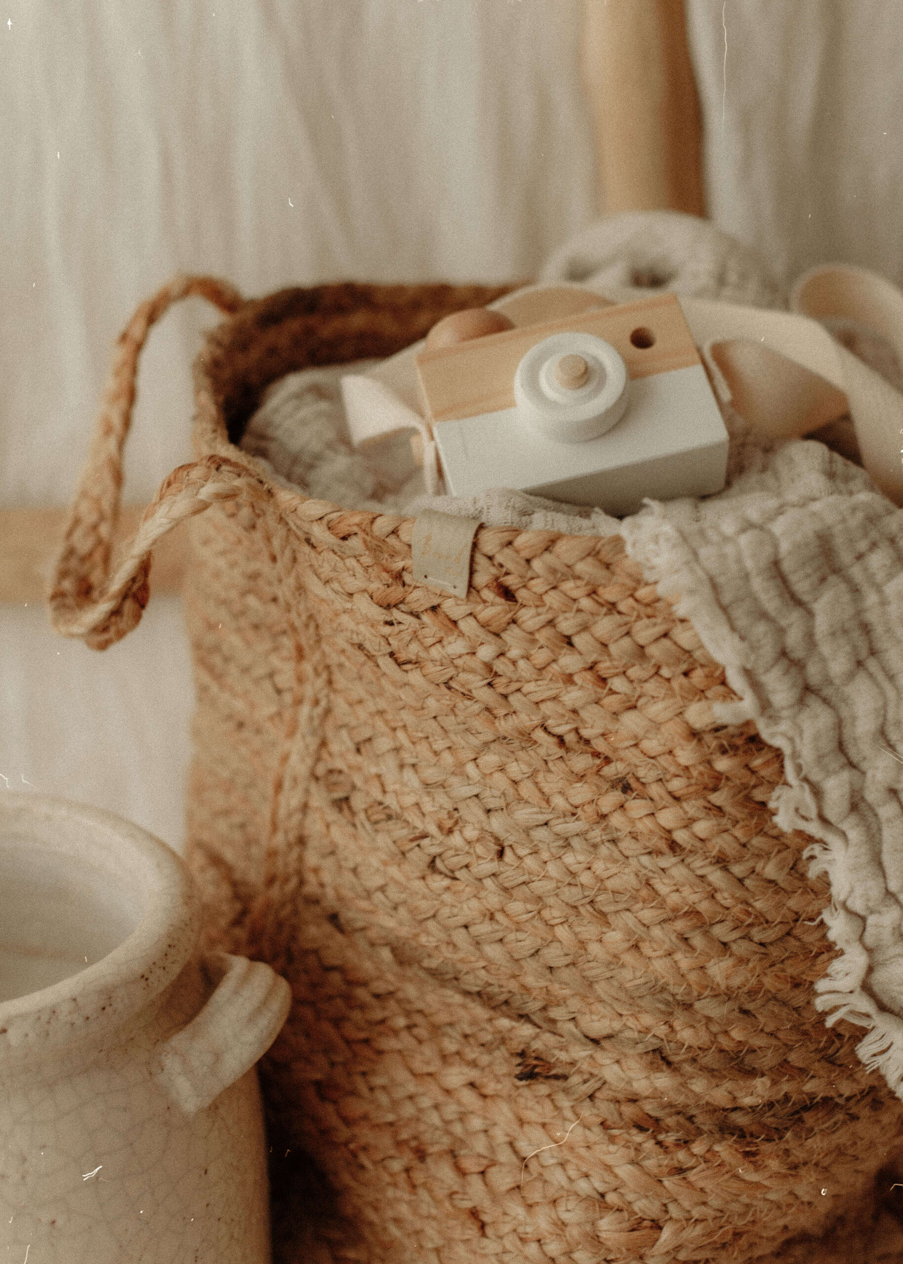 Cream blankets rolled up in a woven basket, topped with a toy wooden camera, in my cotswold photography studio